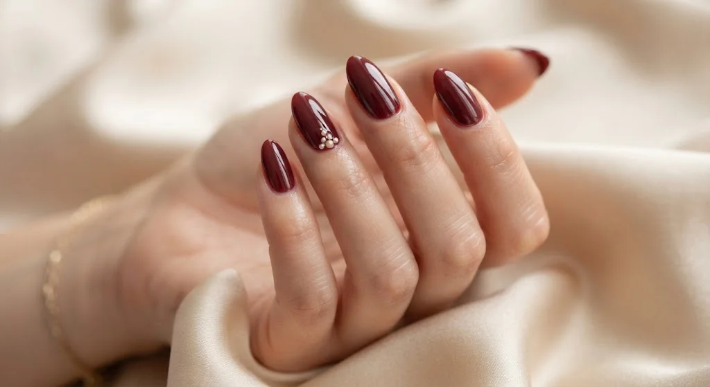 Glossy maroon almond nails with subtle cream pearl accents.